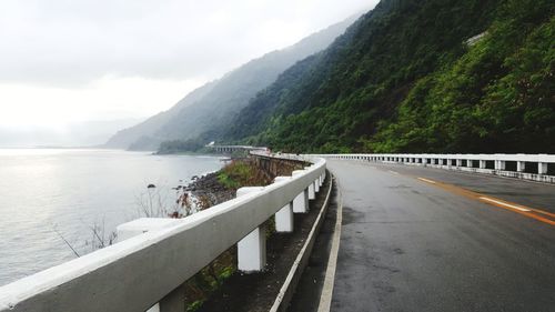 Bridge over road by mountains against sky