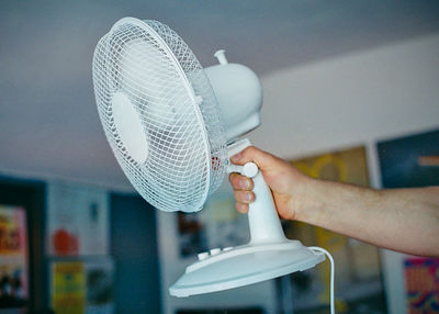 Cropped hand of man holding electric fan at home