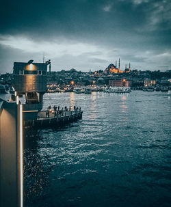 Sailboats in sea by illuminated buildings against sky