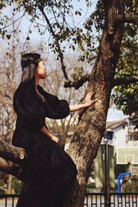 Woman sitting branch touching tree trunk