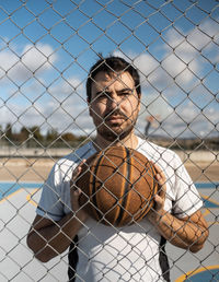 Portrait of young man standing by chainlink fence