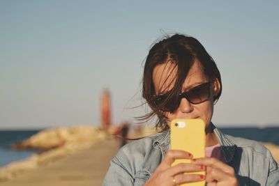 Close-up of young woman using mobile phone at beach against sky