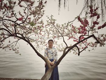 Portrait of smiling teenage girl standing near tree at lakeshore