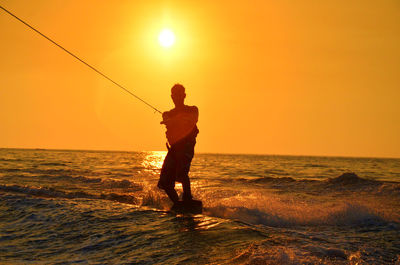 Silhouette man wakeboarding on sea against clear sky