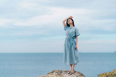 Woman standing on rock by sea against sky