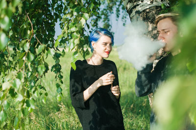 Friends smoking while standing by tree on field