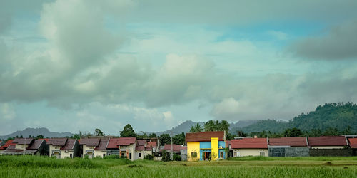 Houses on field by buildings against sky