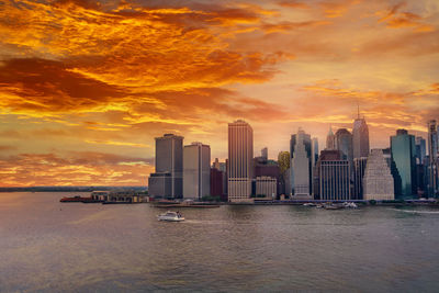 Sea by modern buildings against sky during sunset