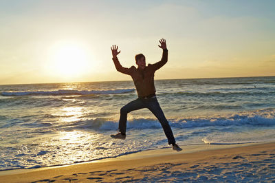 Silhouette of man jumping on beach at sunset