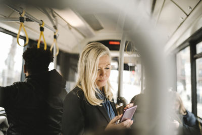 Female professional using smart phone while standing in bus