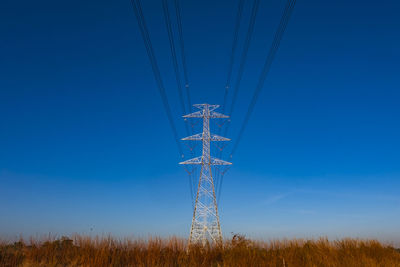 Electric pole and electric cable on the field in the countryside with blue sky.