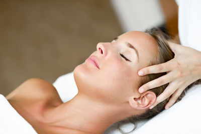 Cropped hand of woman massaging female customer on bed in spa