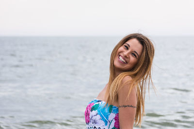 Portrait of smiling young woman at beach against sea and sky