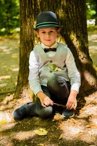 Portrait of boy sitting against tree trunk