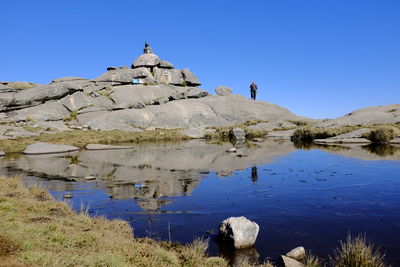 Reflection of rocks in lake against clear blue sky