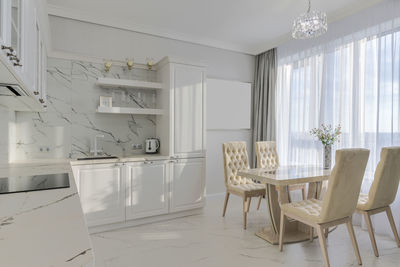 Bright, grey modern kitchen with appliances and dining table by the window. sunlight