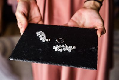 Midsection of woman holding jewelry on slate