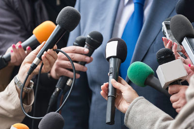 Cropped hands of journalists holding microphones in front of businessman