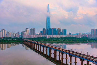 Bridge over river by buildings against sky in city