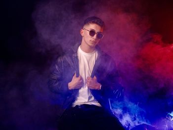 Portrait of young man wearing sunglasses while standing against black background