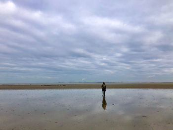 Rear view of woman walking at beach against sky