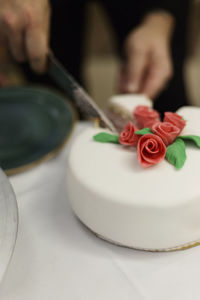 Cropped image of bridegroom cutting wedding cake with red flowers at table