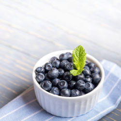 Forest blueberries in white bowl on blue striped napkin on gray wooden background.