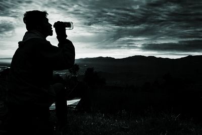 Side view of man sitting on mountain against sky