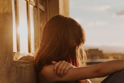 Side view of woman sitting on terrace against sky