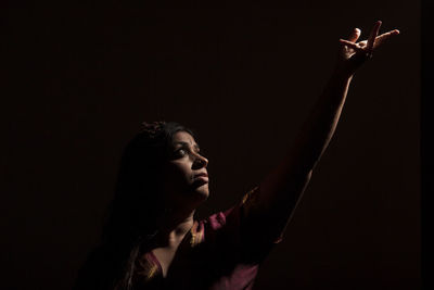 Portrait of young woman looking away against black background