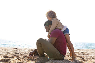 Girl embracing father sitting at beach on sunny day