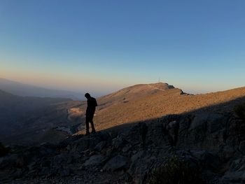 Silhouette man standing on mountain against clear blue sky