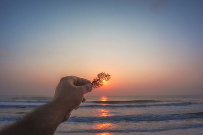 Close-up of hand on sea against sunset sky