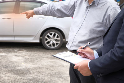 Midsection of salesman discussing with customer while standing by car