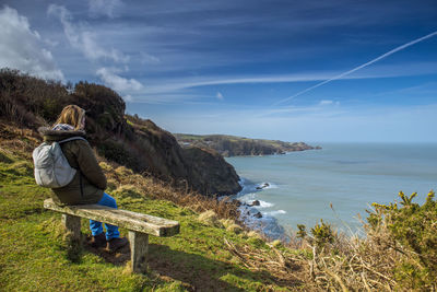 Full length of woman sitting on bench against sea