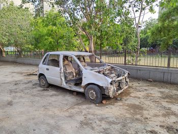 Abandoned car on road against trees in city