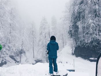 Rear view of woman standing on snow amidst trees during winter