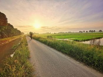 Road amidst field against sky during sunset