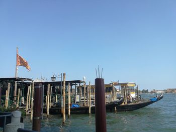 Boats moored in wooden post against clear blue sky