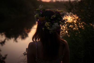 Rear view of woman standing by flowering plants during sunset