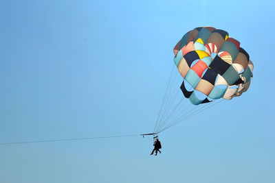 Low angle view of people paragliding against clear blue sky