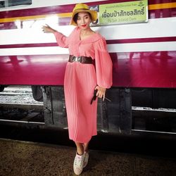 Full length portrait of woman standing against pink wall