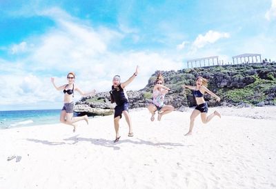 Friends jumping on beach against sky