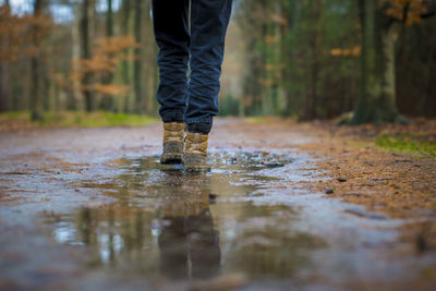 Selective focus shot of hiking boots walking through a puddle of water on a trail in the forest.