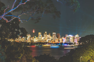 Illuminated buildings by sea against sky at night