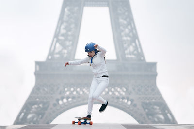 Full length of young woman skateboarding against eiffel tower