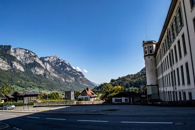 Road by buildings against clear blue sky