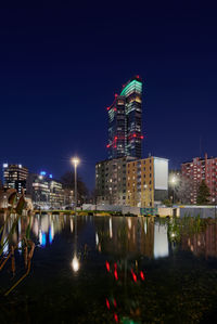 Illuminated buildings by river against sky at night