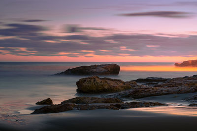 Rocks on beach against sky during sunset