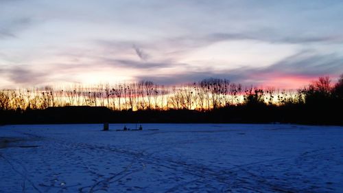 Silhouette trees on snow covered landscape against sky at sunset